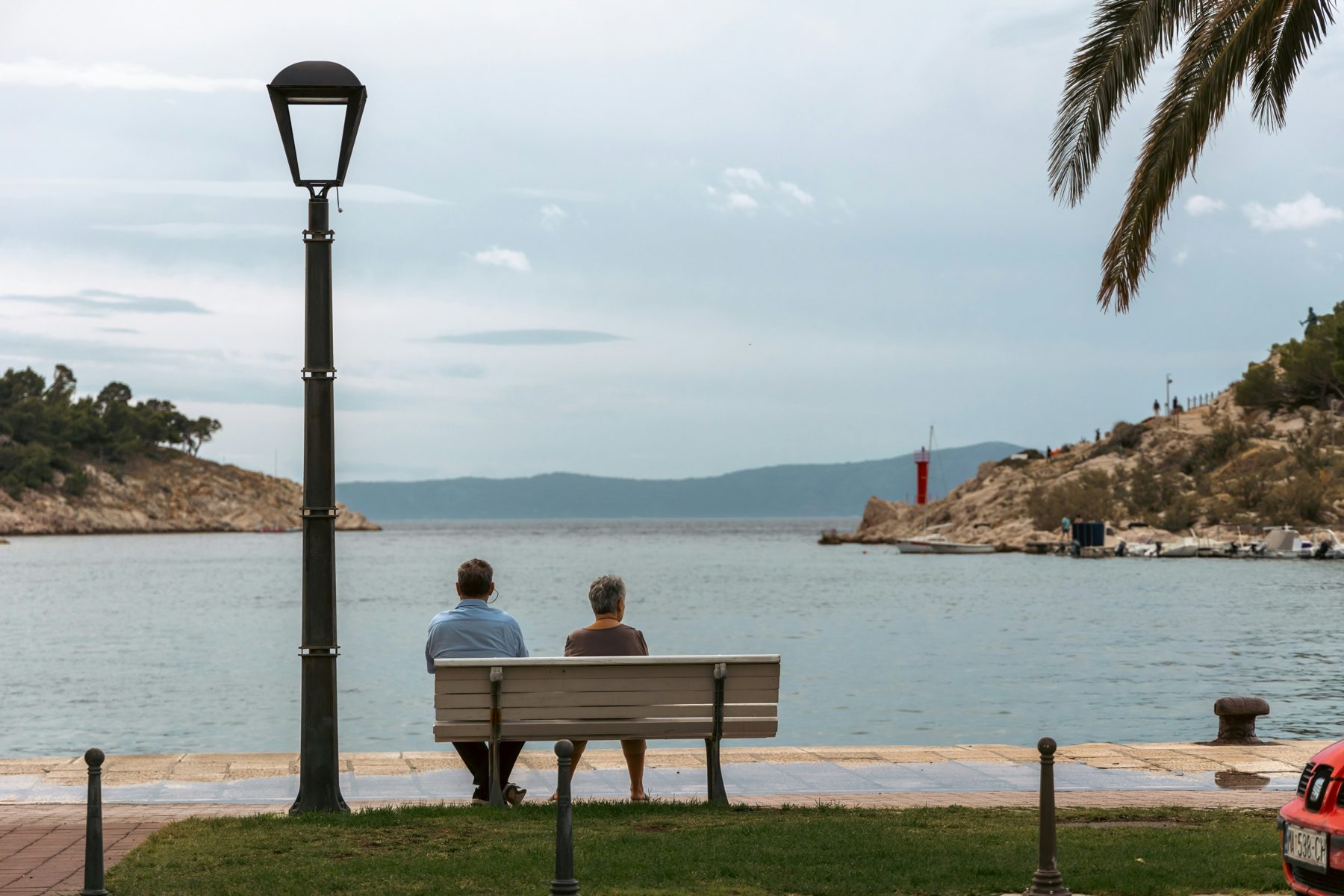 An older couple sitting together on a bench looking out over the Adriatic