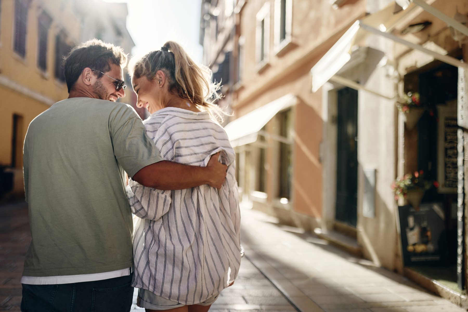 A couple walking arm in arm down a sunlit Croatian street