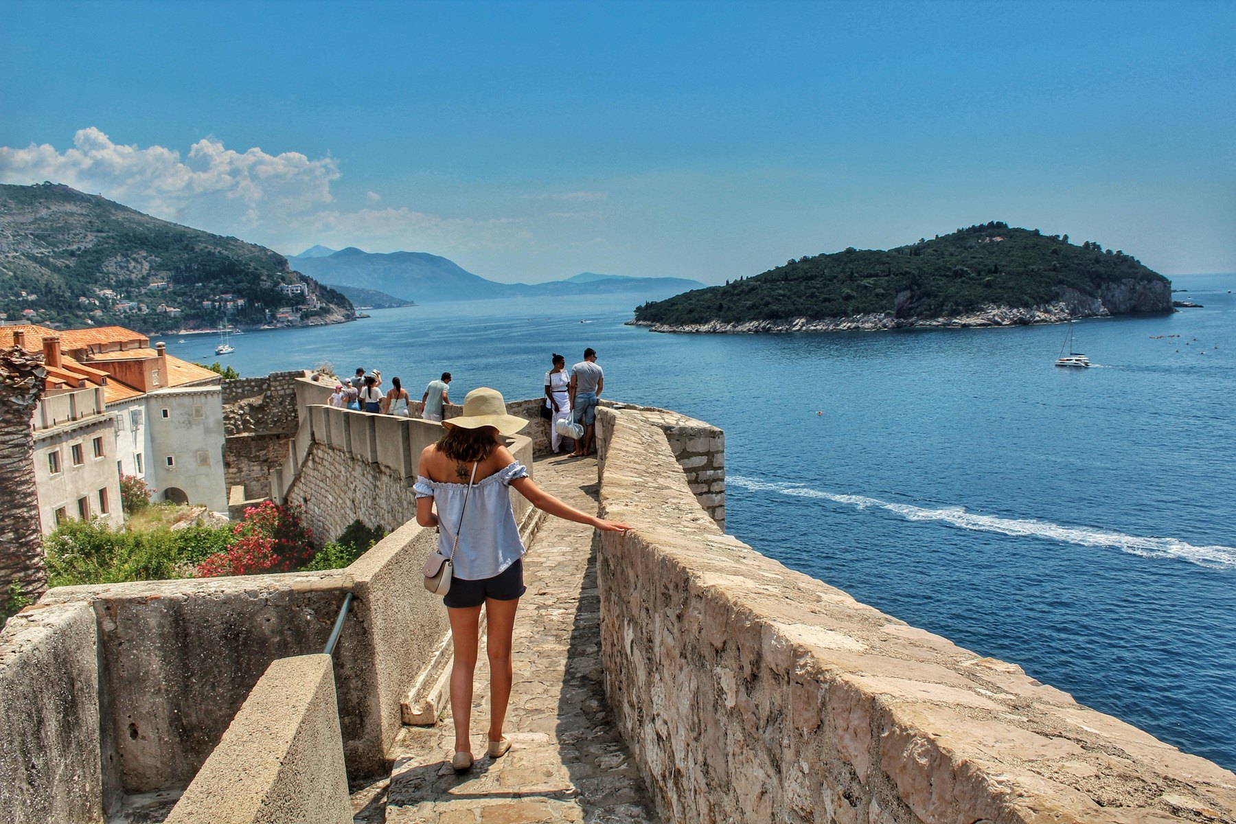 A woman walking along the city walls of Dubrovnik above the sea